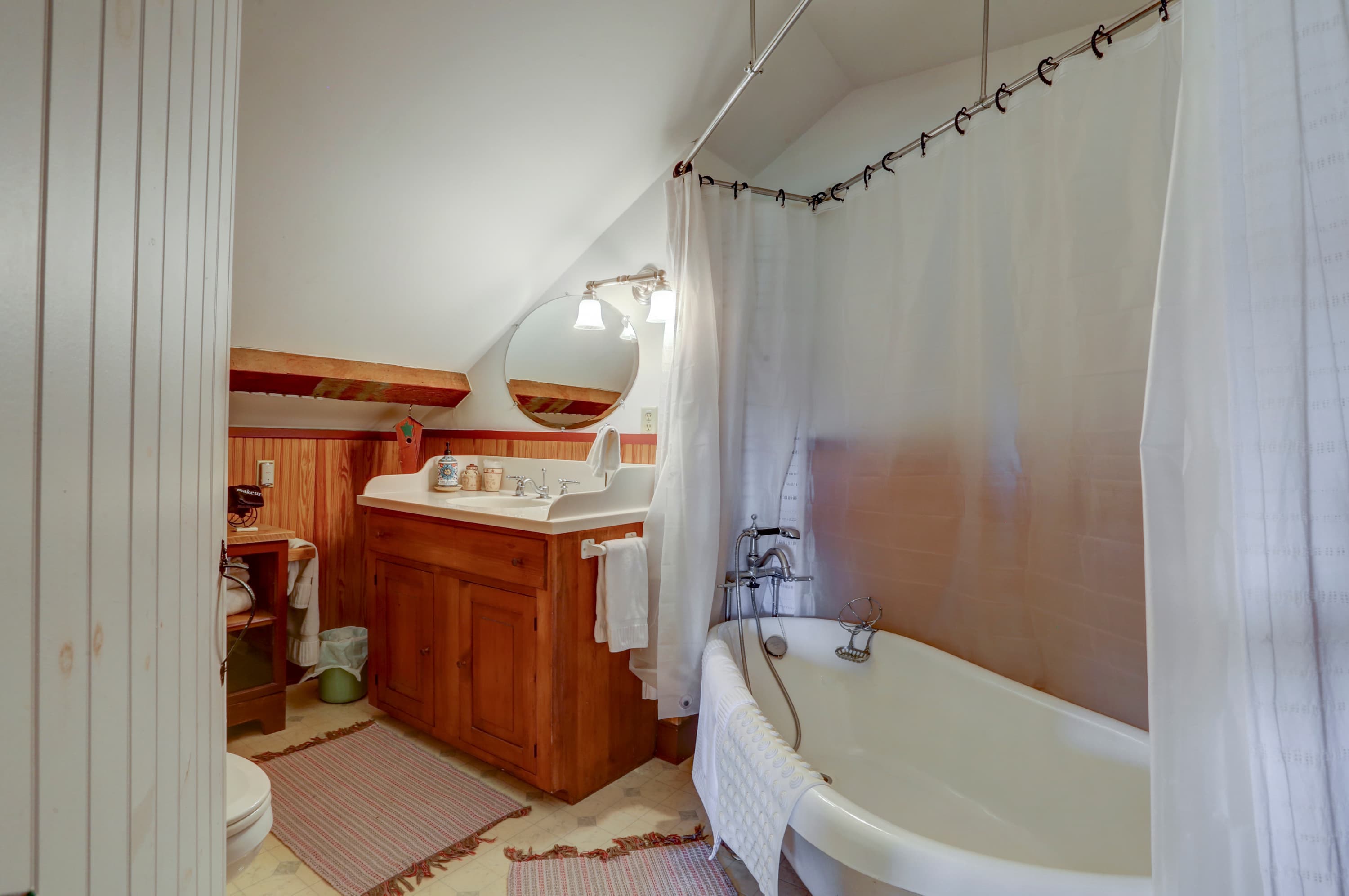 Bathroom with a focus on a clawfoot tub, a wooden vanity with a white towel, and a shower with a white curtain.