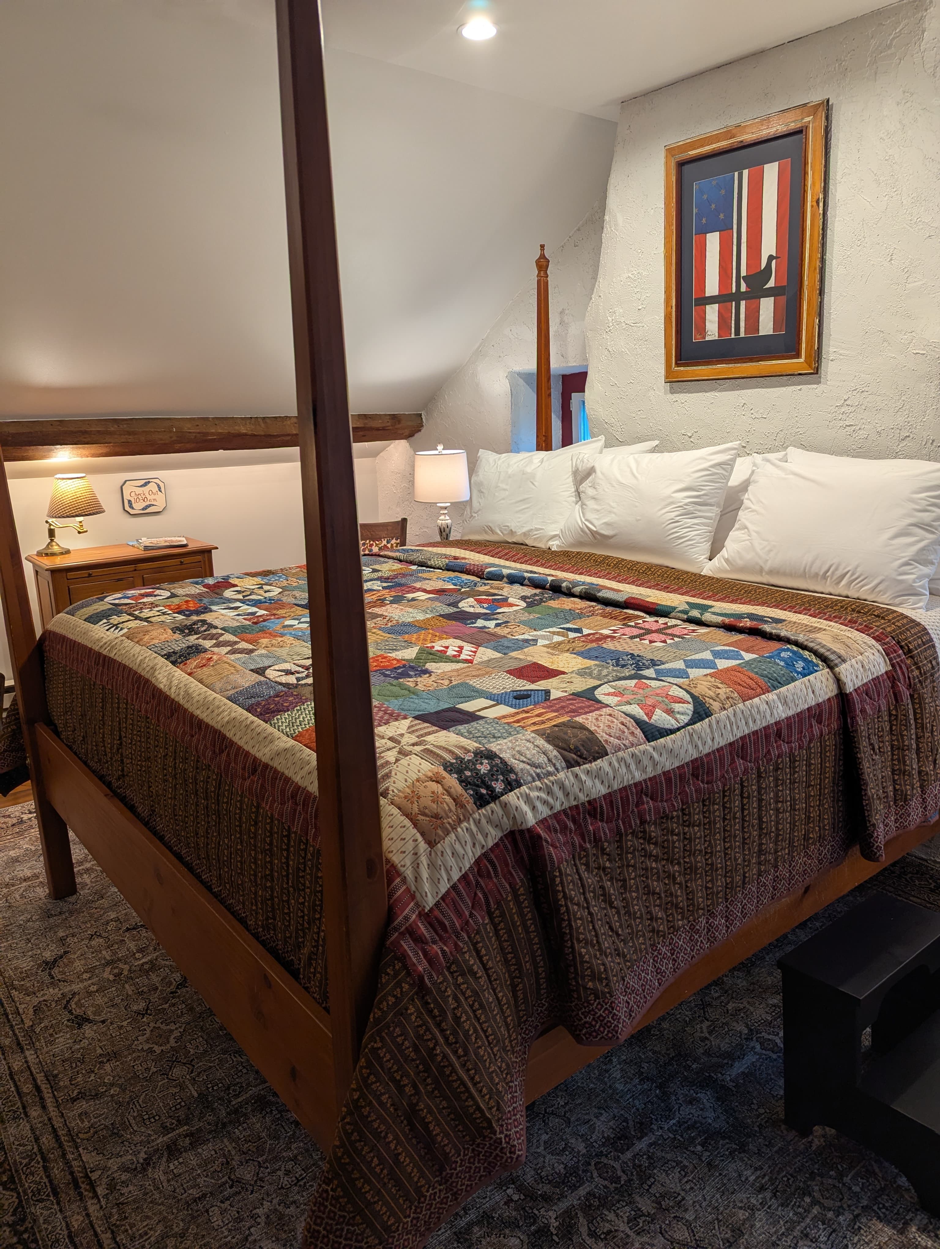 Bedroom scene showing a bed with a Vintage style quilt and an American art pieceon the wall.
