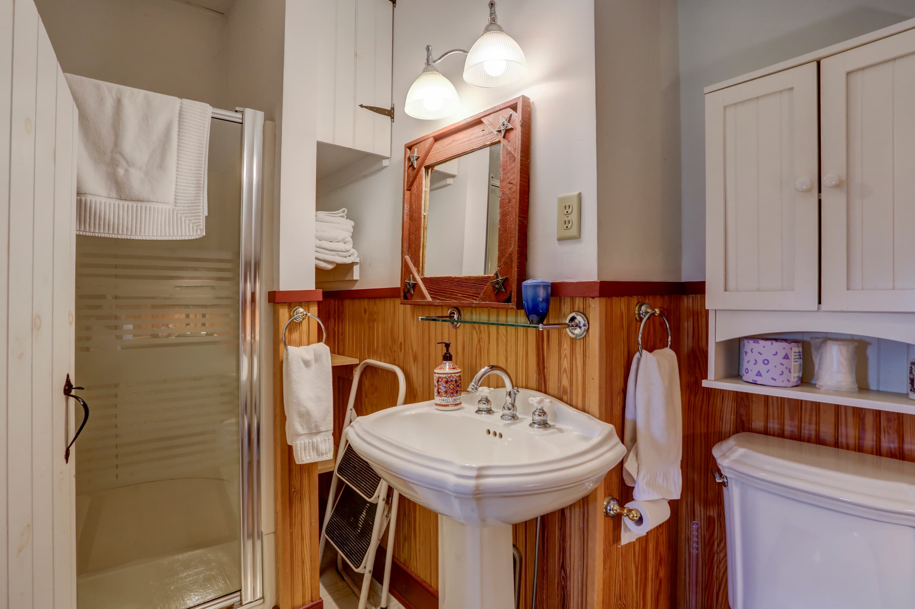 Small bathroom with a focus on a shower with a glass door, a white pedestal sink, and a toilet.