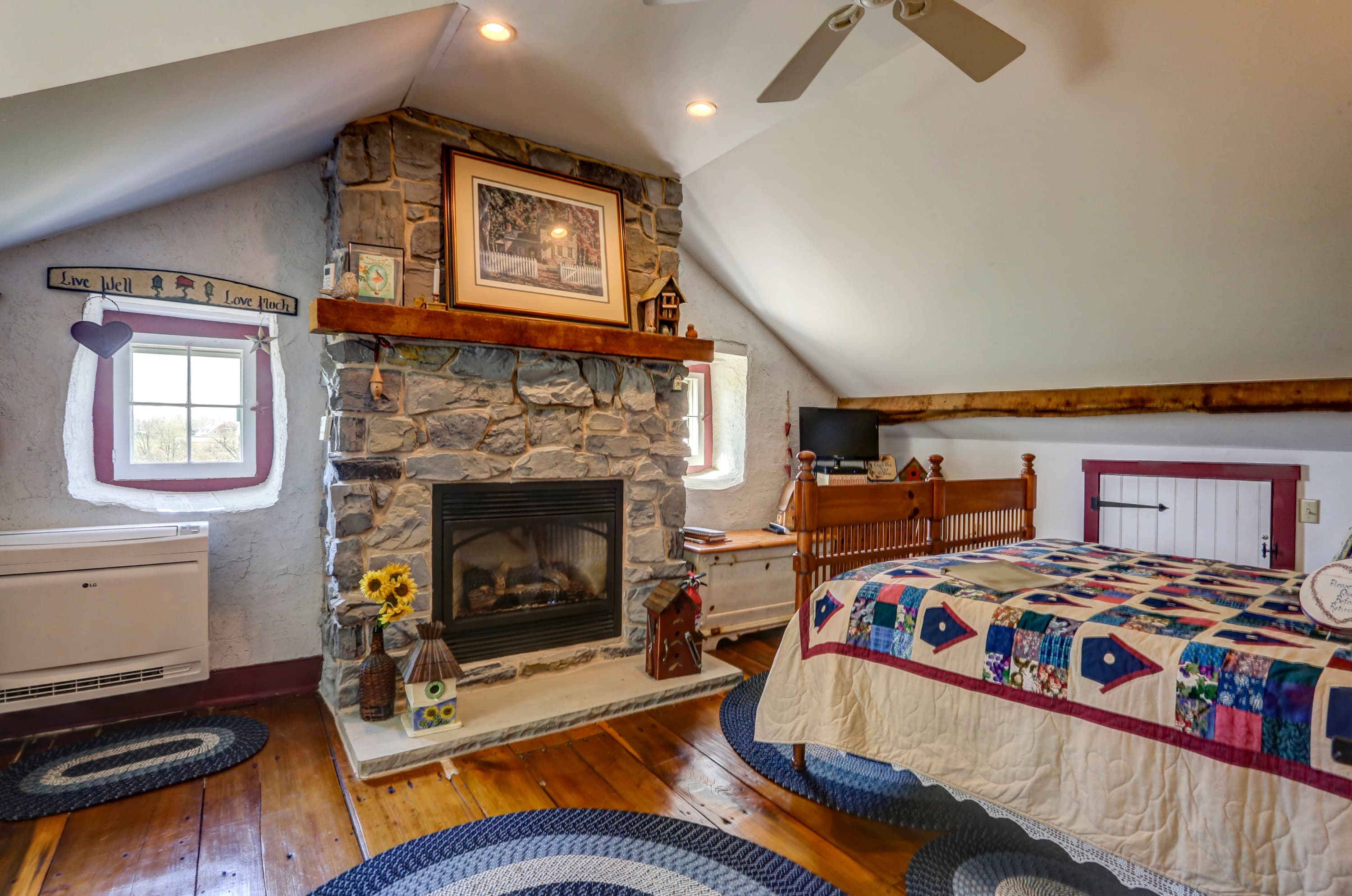 Bedroom with a stone fireplace with a wooden mantel, a bed with a patterned quilt, and a window.