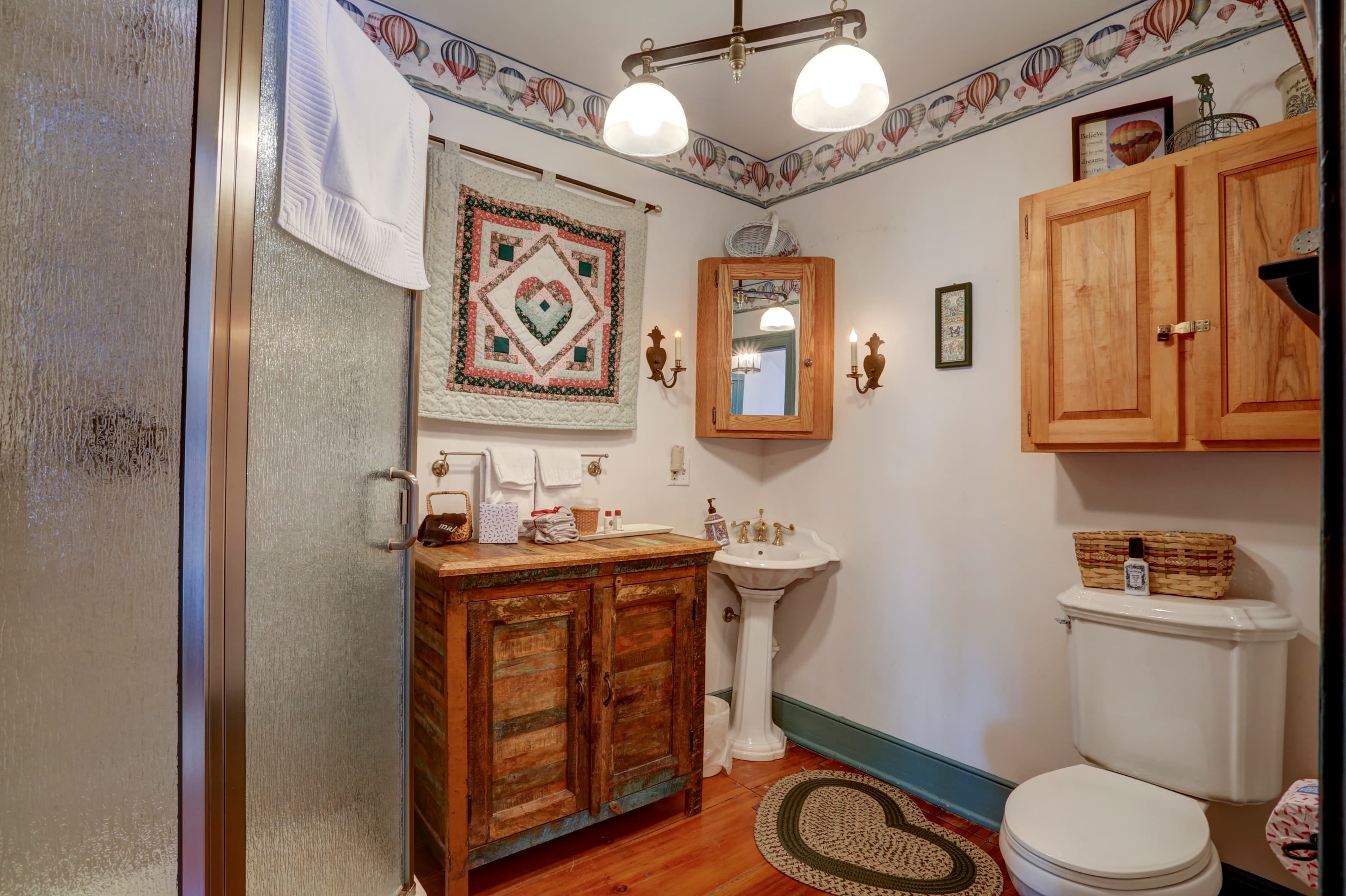 A bathroom with a glass shower door, a wooden vanity with a sink, a toilet, and a patterned rug on the floor.
