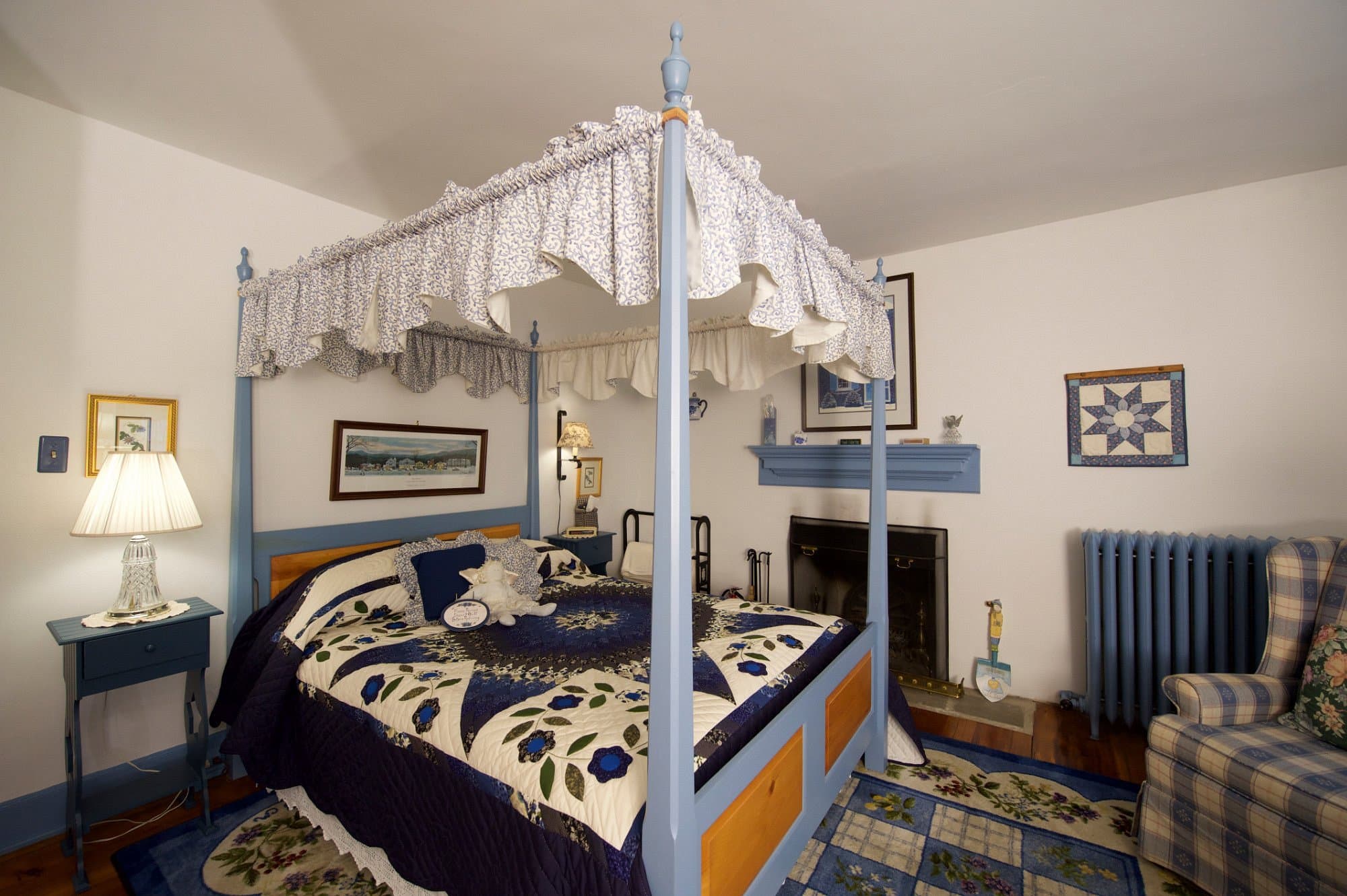 An inviting bedroom with a blue and white four-poster bed with a white canopy, a fireplace with a blue mantel, a blue radiator, and a patterned rug on the floor.
