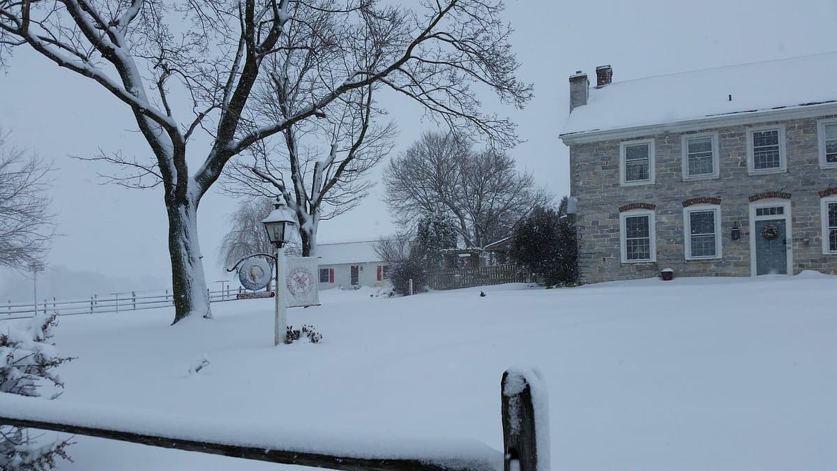 A snowy landscape featuring a historic stone house and bare trees under overcast skies. A snowy landscape featuring a historic stone house and bare trees under overcast skies.
